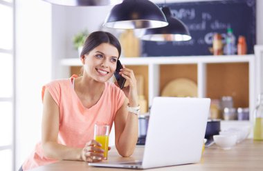 Mutfakta dizüstü bilgisayara benzeyen tariflerle gülümseyen genç bir kadın. Gıda blogcusu kavramı