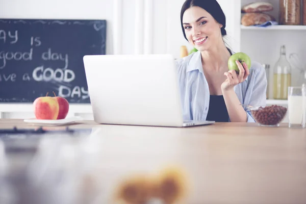 Femme avec pomme et ordinateur portable assis dans la cuisine — Photo