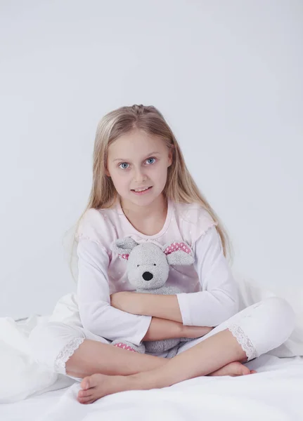 A menina no quarto está sentada na cama. Menina está vestindo um pijama e sentado na cama  . — Fotografia de Stock