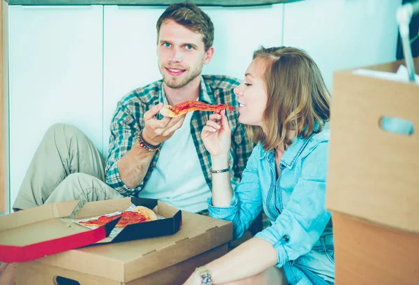 Casal jovem tem uma pausa para o almoço de pizza no chão depois de se mudar para uma nova casa com caixas em torno deles. Casal jovem — Fotografia de Stock