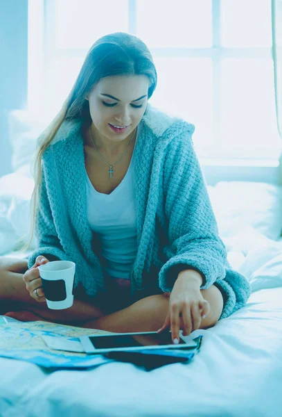 Jeune femme détendue assise sur le lit avec une tasse de café et une tablette numérique — Photo