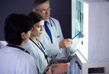 Bir grup doktor bir klinikte röntgenleri inceliyor, teşhis koymayı düşünüyorlar.