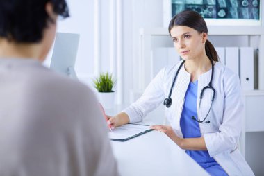 Doktor ve hasta hastane danışma odasında tıbbi sorunları tartışıyorlar. Doktor hasta formunu dolduruyor.