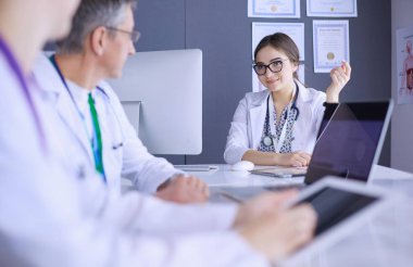 Ciddi bir tıbbi ekip parlak bir ofiste dizüstü bilgisayar kullanıyor.