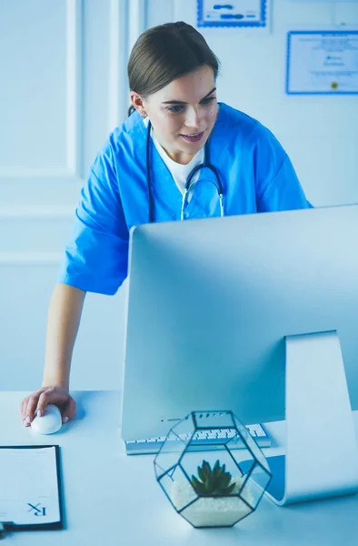 Portrait of female physician filling up medical form while standing near reception desk at clinic or emergency hospital