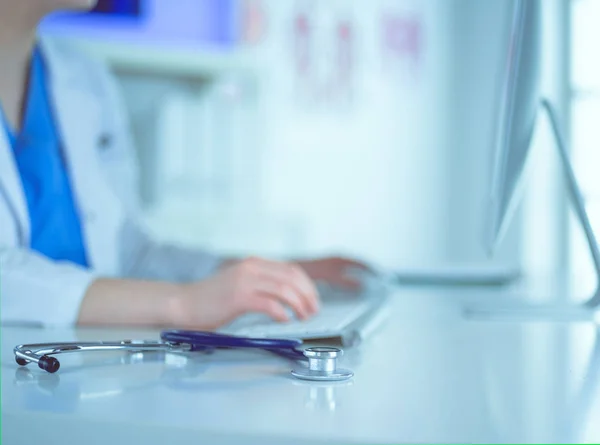 Nahaufnahme eines Stethoskops liegt auf dem Tisch neben Ärztin, die am Laptop tippt — Stockfoto