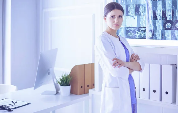 Προσωπογραφία νεαρής γυναίκας γιατρού με λευκό παλτό που στέκεται στο νοσοκομείο με σταυρωμένα τα χέρια — Φωτογραφία Αρχείου