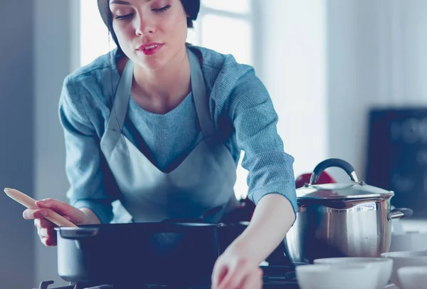 Mujer parada junto a la estufa en la cocina, cocinando y oliendo los agradables aromas  . — Foto de Stock