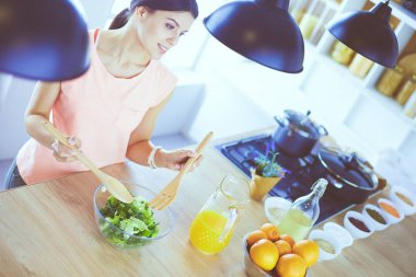 Gülümseyen genç kadın mutfakta taze salata karıştırıyor..