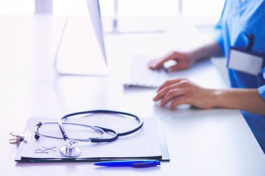 Kadın doktor masada oturuyor ve hastanede dizüstü bilgisayarla çalışıyor.