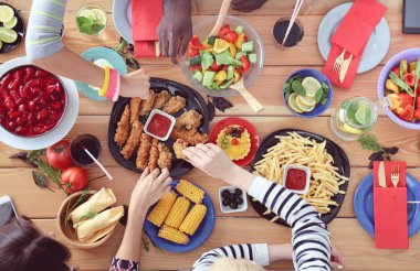 Ahşap masada otururken birlikte yemek yiyen bir grup insanın üst düzey görüntüsü. Masada yemek var. İnsanlar fast food yiyor..