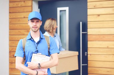 Mavi üniformalı gülümseyen kurye servis konseptine paket kutusu teslim eden teslimatçı. Mavi üniformalı gülümseyen teslimatçı.