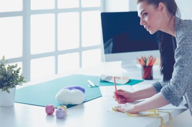 Moda tasarımcıları stüdyoda çalışıyor, masanın yanında duruyorlar.