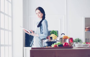 Mutfakta yemek yapmak için tablet bilgisayar kullanan genç bir kadın.