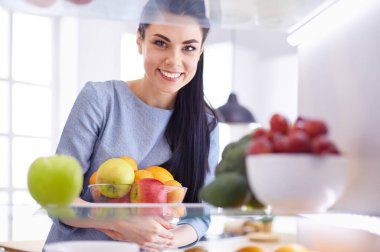 Gülümseyen kadın buzdolabından taze meyve alıyor, sağlıklı yiyecek konsepti.