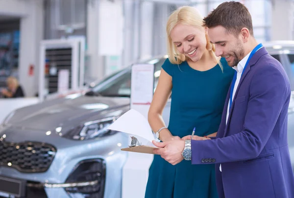 Car salesman sells a car to happy customer in car dealership and hands over the keys