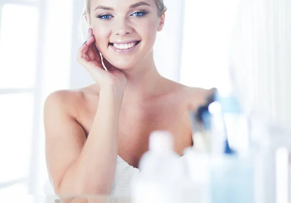 Mujer joven en albornoz mirando en el espejo del baño — Foto de Stock