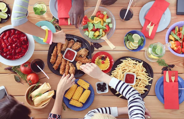 Ahşap masada otururken birlikte yemek yiyen bir grup insanın üst düzey görüntüsü. Masada yemek var. İnsanlar fast food yiyor..