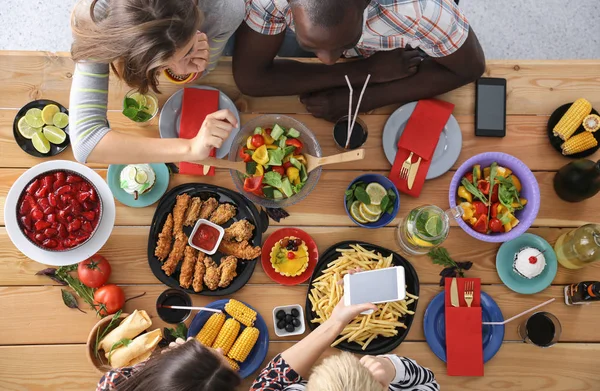 Ahşap masada otururken birlikte yemek yiyen bir grup insanın üst düzey görüntüsü. Masada yemek var. İnsanlar fast food yiyor..