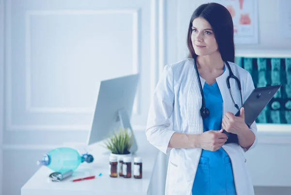 Vacker läkare stående i ett konsult rum med en mapp i hennes händer, tänkande — Stockfoto