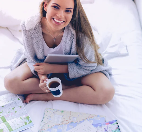 Entspannte junge Frau sitzt mit einer Tasse Kaffee und digitalem Tablet im Bett — Stockfoto