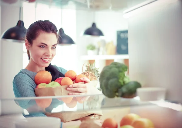 Mujer sonriente sacando una fruta fresca de la nevera, concepto de comida saludable —  Fotos de Stock