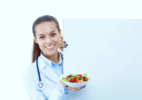 Portrait d'une belle femme médecin tenant une assiette avec des légumes frais debout près de blanc. Femmes médecins — Photo