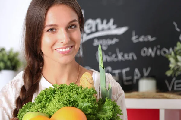Mutfakta elinde sebzelerle gülümseyen genç bir kadın. Gülümseyen genç kadın