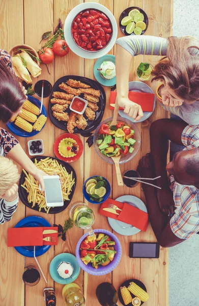 Ahşap masada otururken birlikte yemek yiyen bir grup insanın üst düzey görüntüsü. Masada yemek var. İnsanlar fast food yiyor..