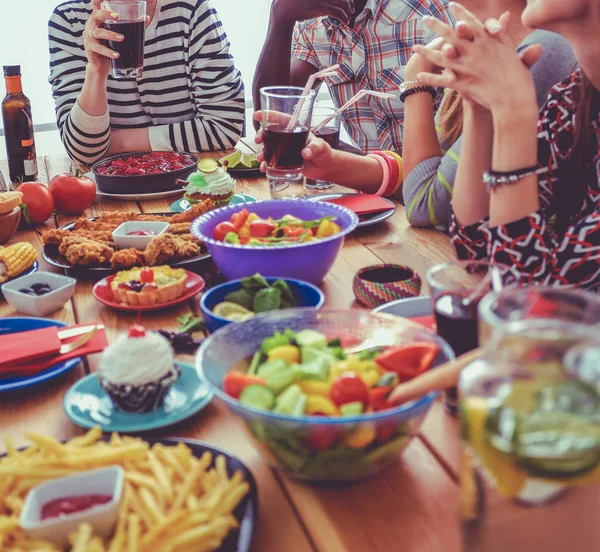Ahşap masada otururken birlikte yemek yiyen bir grup insanın üst düzey görüntüsü. Masada yemek var. İnsanlar fast food yiyor..