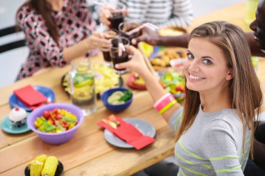 Ahşap masada otururken birlikte yemek yiyen bir grup insanın üst düzey görüntüsü. Masada yemek var. İnsanlar fast food yiyor. Bir kızın portresi.