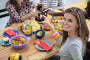 Ahşap masada otururken birlikte yemek yiyen bir grup insanın üst düzey görüntüsü. Masada yemek var. İnsanlar fast food yiyor. Bir kızın portresi.