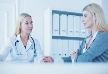 Hasta bir tıbbi Danışma alma ve kameraya bakarak gülen, kadın doktor masada oturuyor