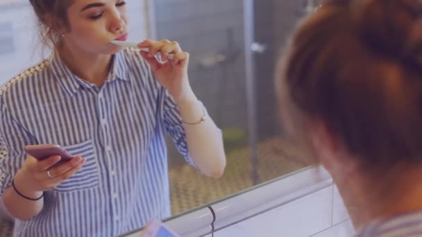 Menina escovando dentes e usando o telefone móvel — Vídeo de Stock