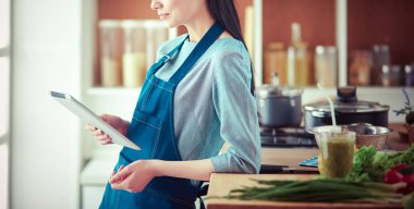 Mutfakta yemek yapmak için tablet bilgisayar kullanan genç bir kadın.