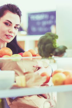 Gülümseyen kadın buzdolabından taze meyve alıyor, sağlıklı yiyecek konsepti.