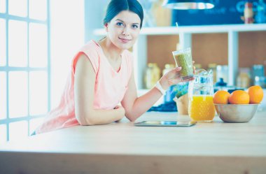 Mutfakta dijital tablet kullanan güzel genç bir kadın.