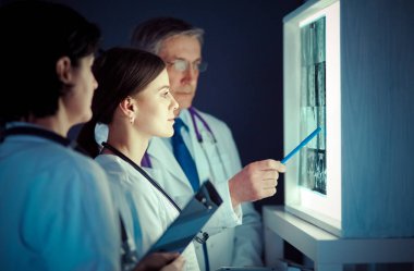 Bir grup doktor bir klinikte röntgenleri inceliyor, teşhis koymayı düşünüyorlar.