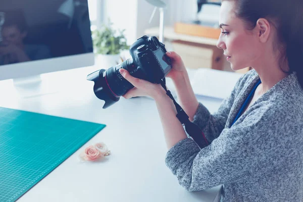 Jonge vrouw ontwerper staat in de buurt van de werkplek en fotograferen op digitale camera — Stockfoto