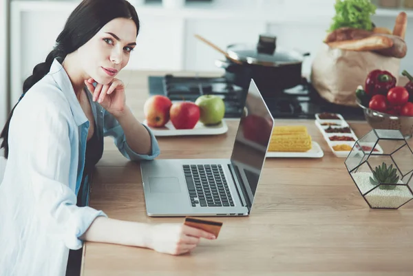 Donna sorridente shopping online con computer e carta di credito in cucina — Foto Stock