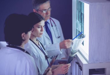 Bir grup doktor bir klinikte röntgenleri inceliyor, teşhis koymayı düşünüyorlar.