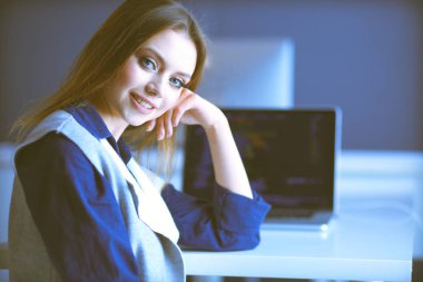 Ofis masasında çalışan ve dizüstü bilgisayarla yazan kendine güvenen genç bir iş kadını.