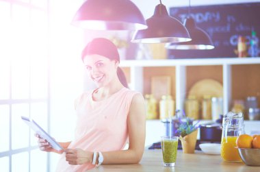 Mutfakta dijital tablet kullanan güzel genç bir kadın.