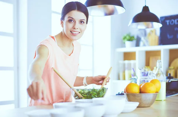 Leende ung kvinna blandar färsk sallad i köket. — Stockfoto