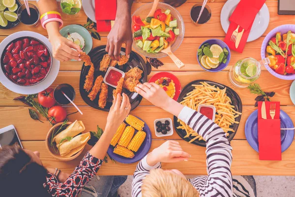 Top view of group of people having dinner together while sitting at wooden table. Food on the table. People eat fast food. — Stock Photo, Image