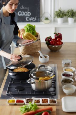 Mutfakta yemek yapmak için tablet bilgisayar kullanan genç bir kadın.