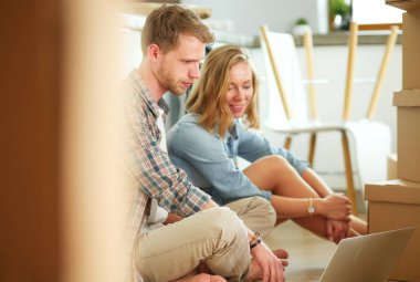 Genç bir çift yeni ev içinde hareket. Oturma ve açma sonra rahatlatıcı. Bir şey üstünde laptop arıyorum. Genç Çift