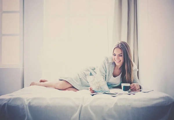 Relaxado jovem mulher sentada na cama com uma xícara de café e tablet digital — Fotografia de Stock