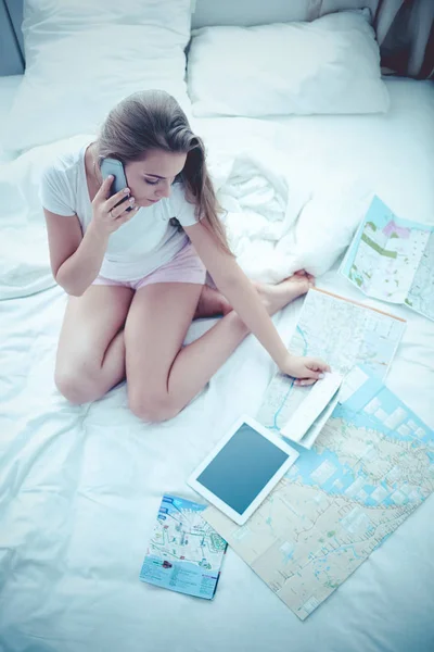 Расслабленная молодая женщина сидит на кровати с чашкой кофе и цифровой планшет — стоковое фото