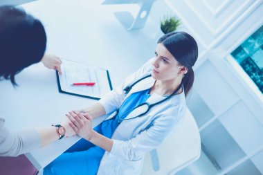 Kadın doktor hastane danışma odasında bir hastayı sakinleştiriyor, elini tutuyor.